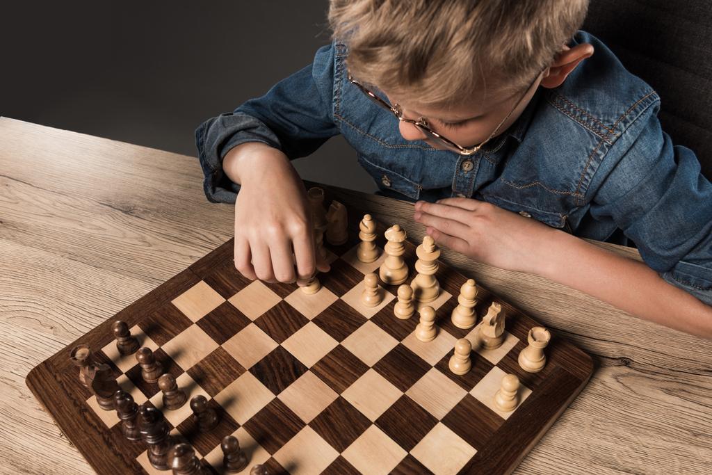 pohled z malého chlapce v brýlích hraje šachy u stolu  - Fotografie, Obrázek