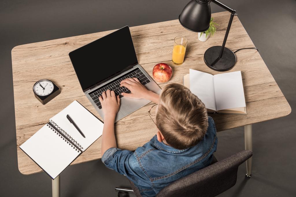 vista aérea do estudante fazendo lição de casa no laptop à mesa com livro didático, livro, planta, lâmpada, relógio, maçã e copo de suco
  - Foto, Imagem
