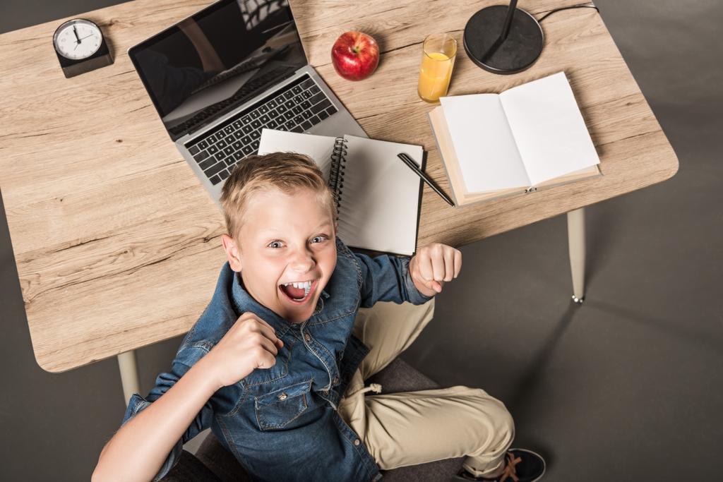 vista aérea do estudante animado gesticulando por mãos à mesa com laptop, livro, livro didático, maçã, suco, lâmpada e relógio
  - Foto, Imagem