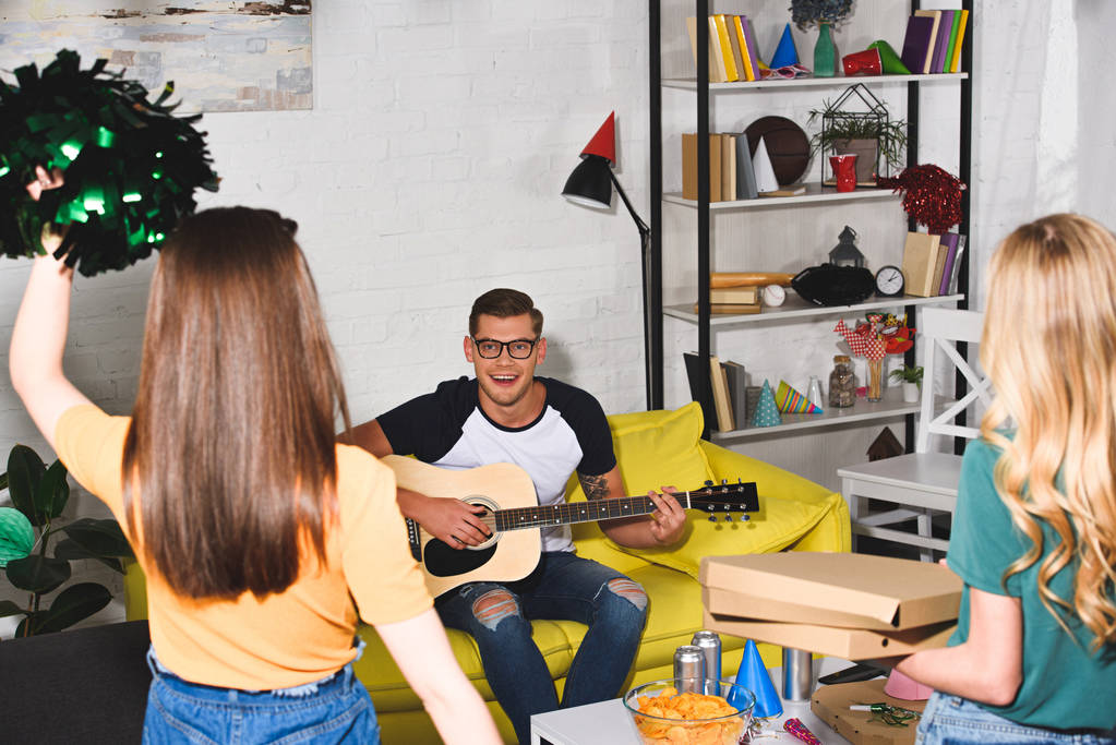 lányok, pizzás dobozok és néztem mosolygó ember gitározni otthoni partin pom-poms hátulnézete - Fotó, kép