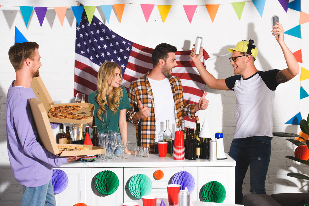 nuori mies, jolla on laatikoita pizzalla ja katselee onnellisia ystäviä juomassa alkoholijuomia ja juhlimassa yhdessä
 - Valokuva, kuva
