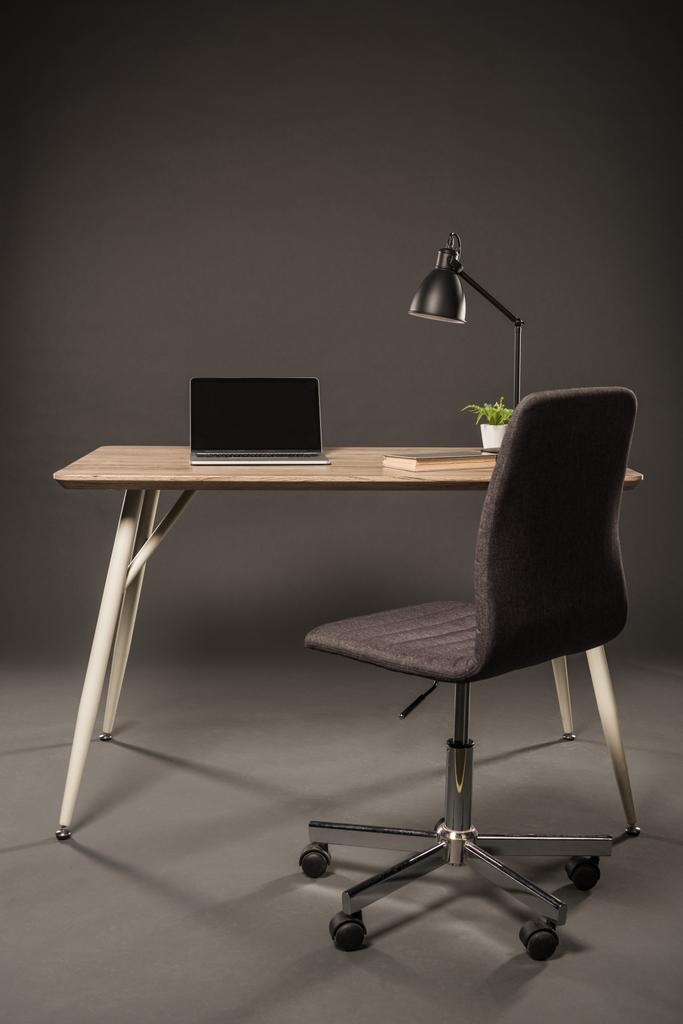 Stuhl und Tisch mit Lampe, Pflanze, Buch und Laptop mit leerem Bildschirm auf grauem Hintergrund  - Foto, Bild