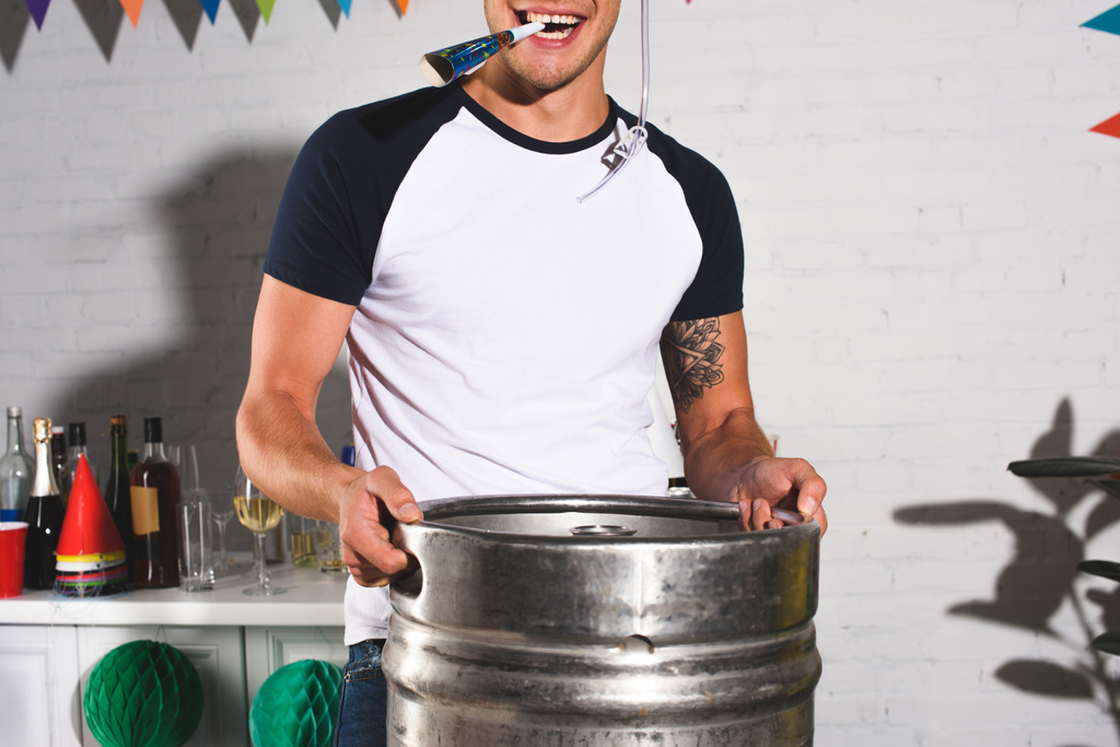 обрезанный снимок счастливого молодого человека, держащего бочку пива на домашней вечеринке
 - Фото, изображение