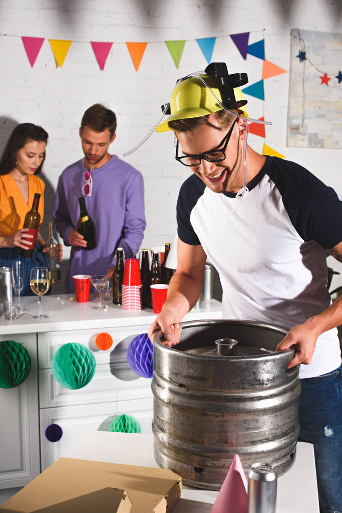 smiling young man holding beer barrel while friends drinking behind - Photo, Image