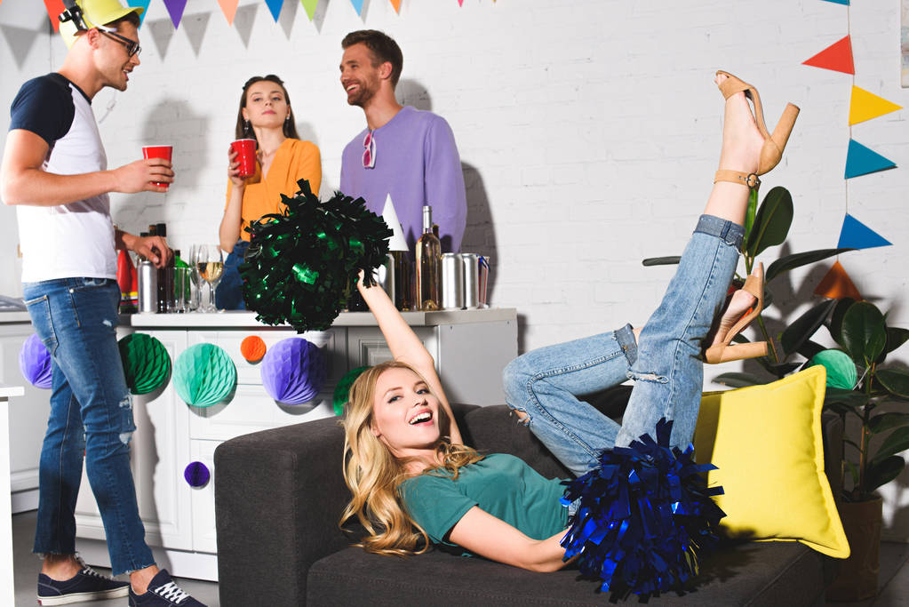 happy young woman lying on couch while cheerful friends partying behind - Photo, Image