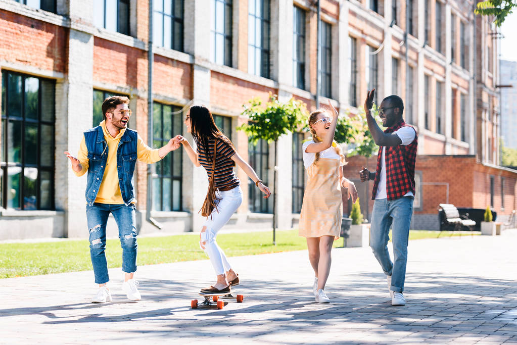 happy multiracial friends with long board having fun while spending time together on street - Photo, Image