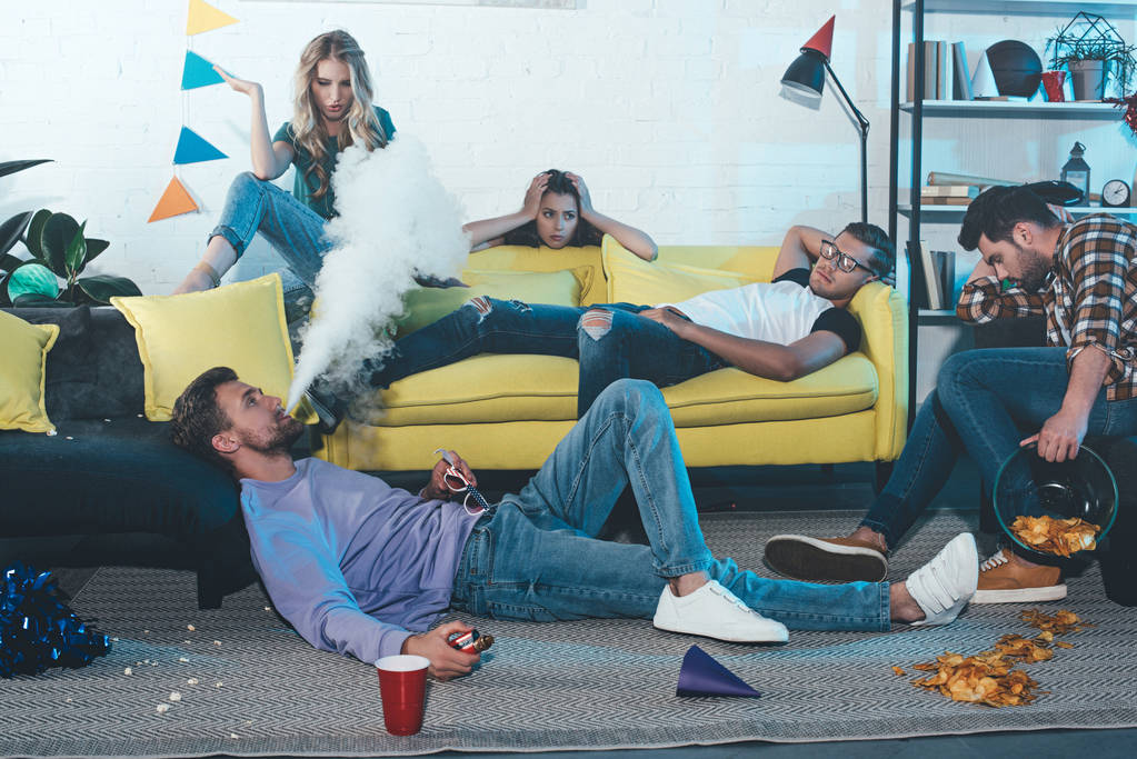 man smoking electronic cigarette and blowing smoke while partying with drunk friends - Photo, Image