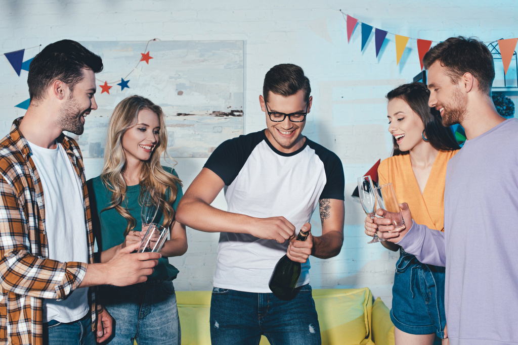 glückliche junge Freundinnen und Freunde öffnen eine Flasche Wein auf der Heimparty  - Foto, Bild