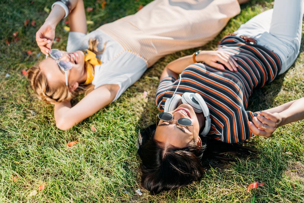 mujeres sonrientes jóvenes multiculturales descansando sobre hierba verde en el parque
 - Foto, imagen