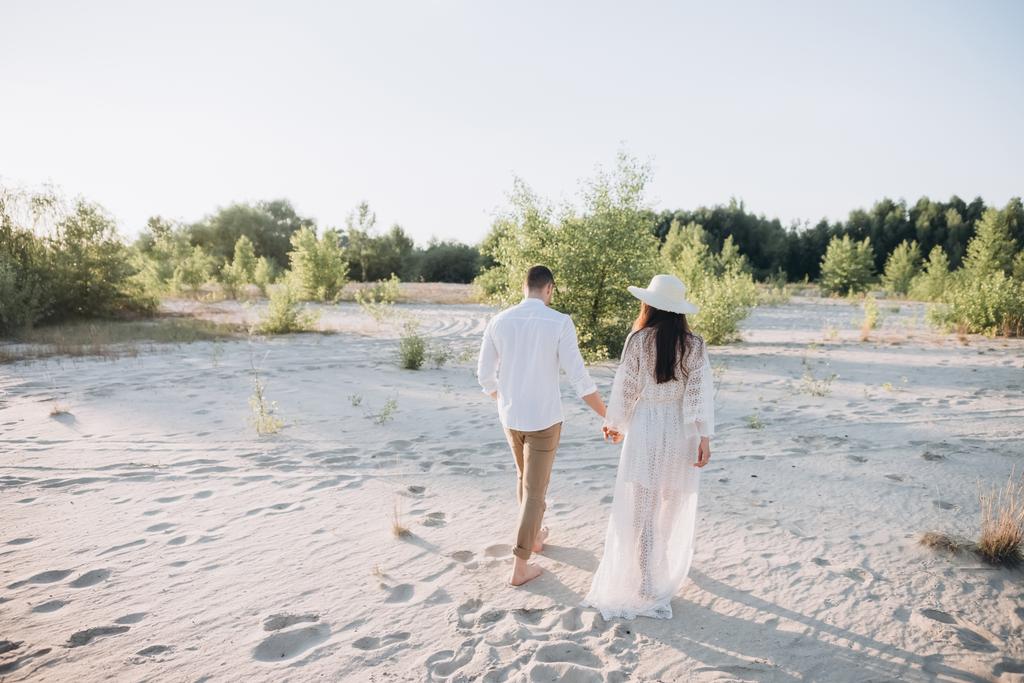 zadní pohled na páru, drželi se za ruce a chůzi na pláži - Fotografie, Obrázek