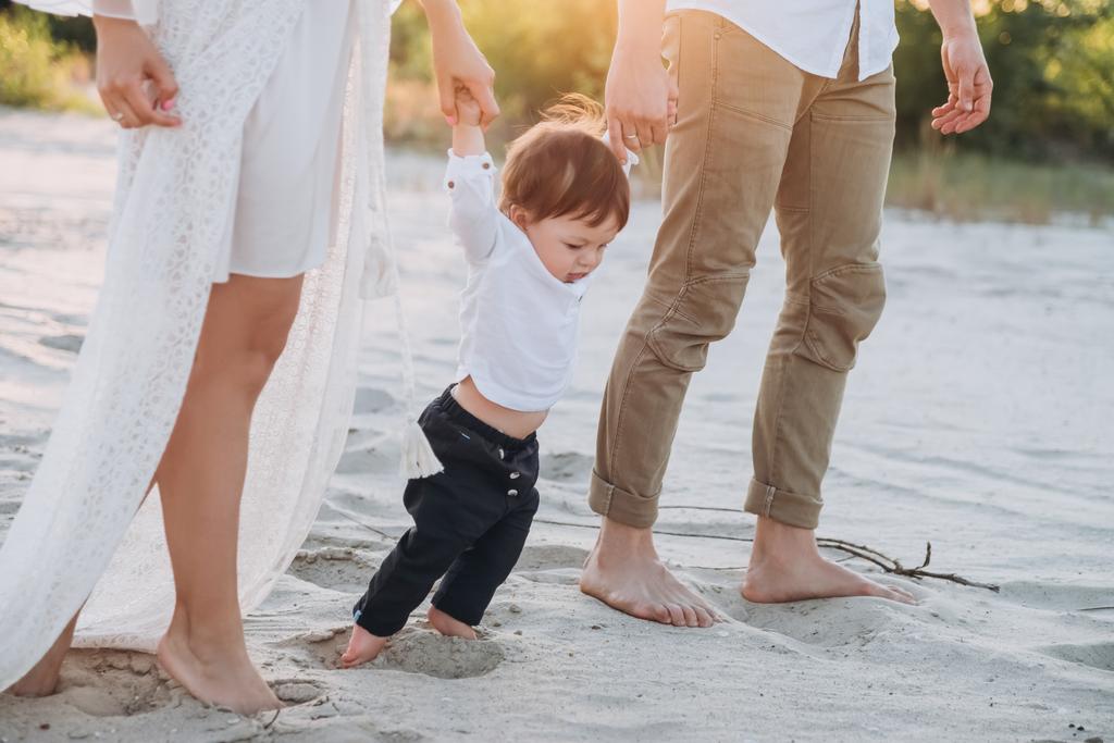 Οι γονείς, κρατώντας τα χέρια με το αξιολάτρευτο γιο σε αμμώδη παραλία - Φωτογραφία, εικόνα