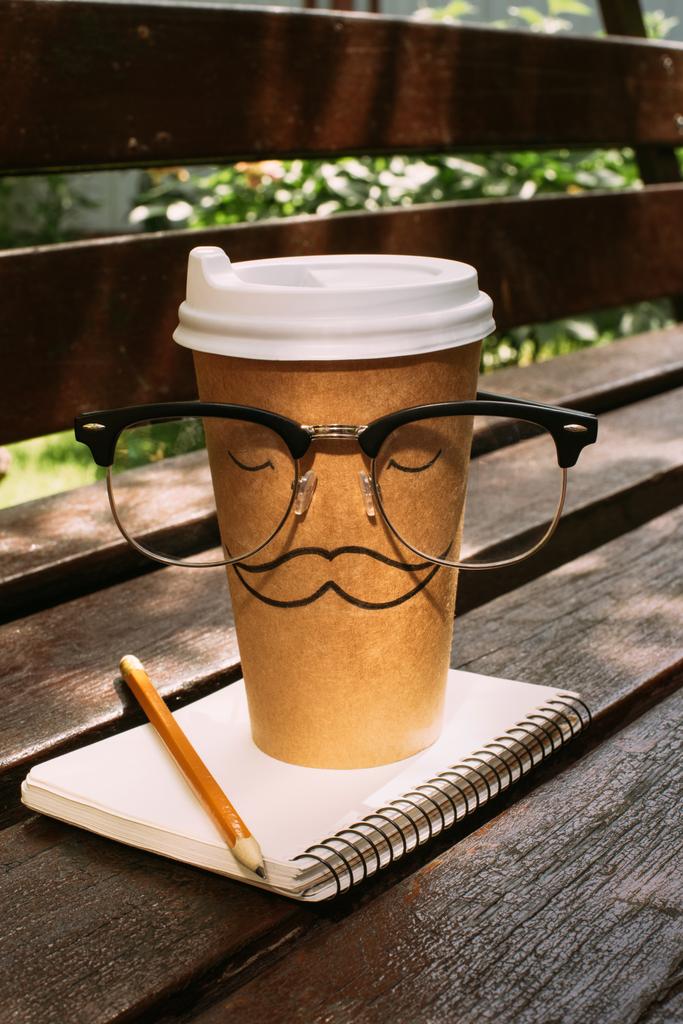 primer plano vista de café para ir con anteojos, cuaderno y lápiz en banco de madera
 - Foto, Imagen