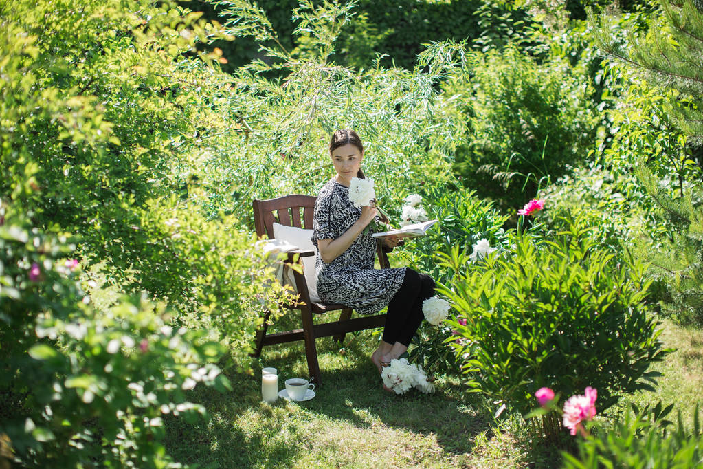 若い女性はお茶のマグと椅子に庭で休憩します。 - 写真・画像