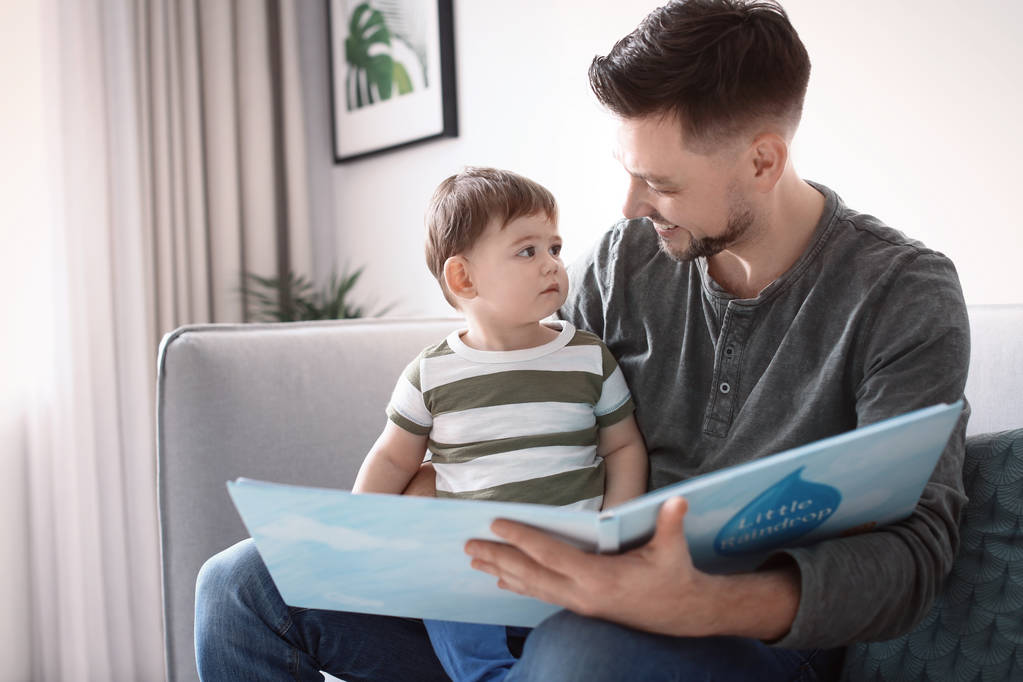 Papà e suo figlio leggono un libro sul divano a casa
 - Foto, immagini