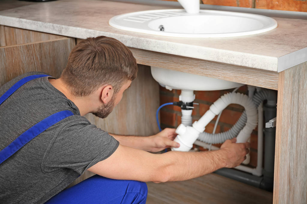 Professional plumber in uniform fixing sink indoors - Photo, Image