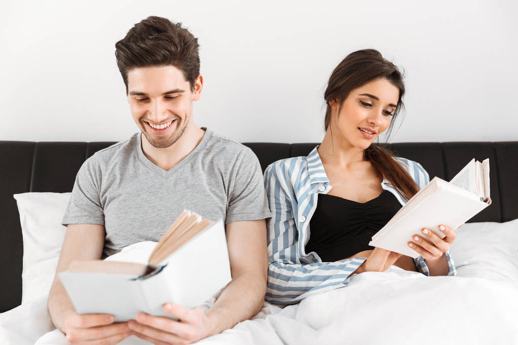Щаслива молода пара читає книги, сидячи разом у ліжку
 - Фото, зображення