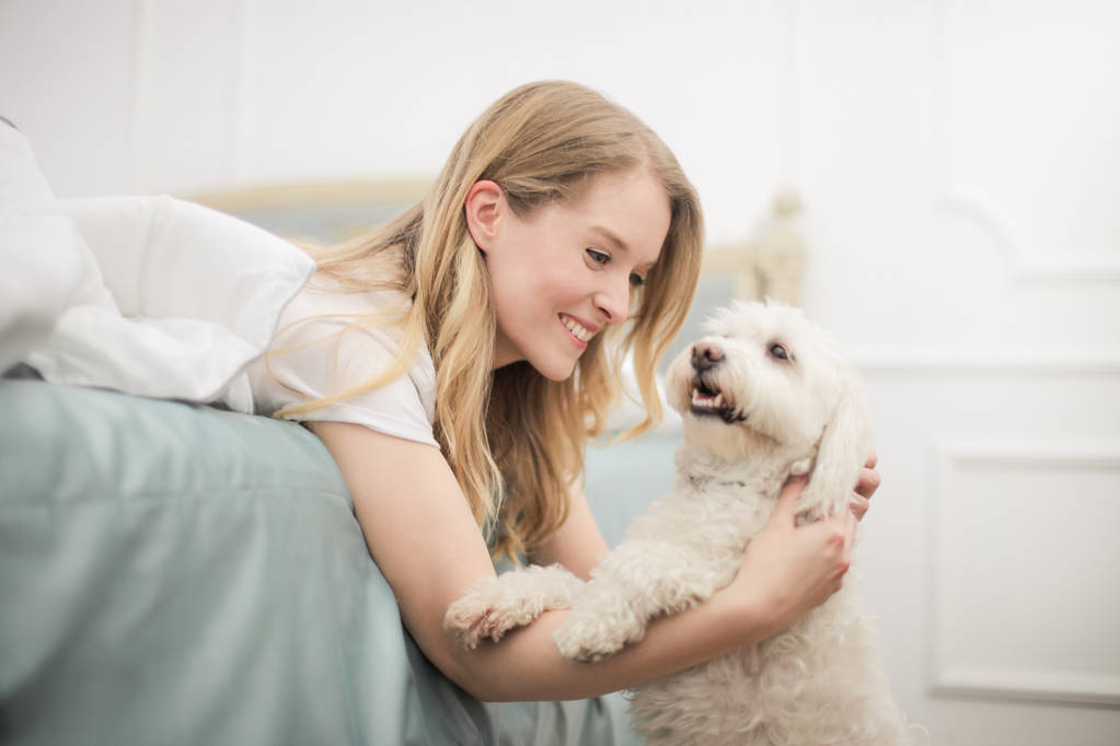 junge schöne blonde Frau liegt auf ihrem Bett und spielt mit ihrem süßen Hund. - Foto, Bild