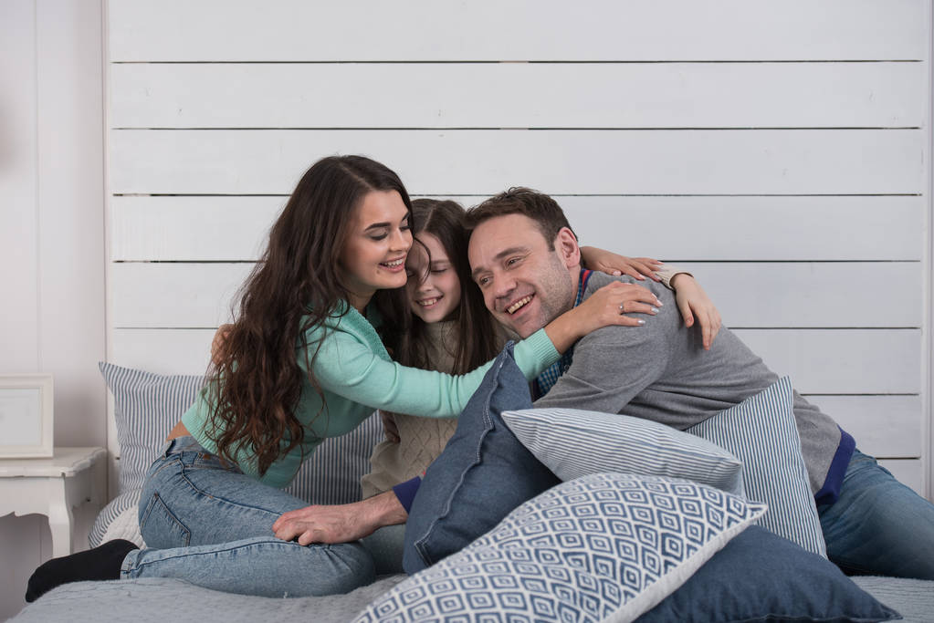 Retrato familiar de padres felices y su hija abrazándose en la cama en casa
 - Foto, Imagen