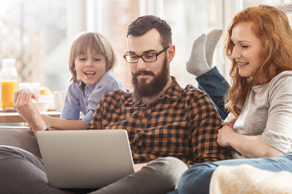Szczęśliwa rodzina razem oglądania filmu. Człowiek z laptopa między uśmiechający się syn i żona - Zdjęcie, obraz