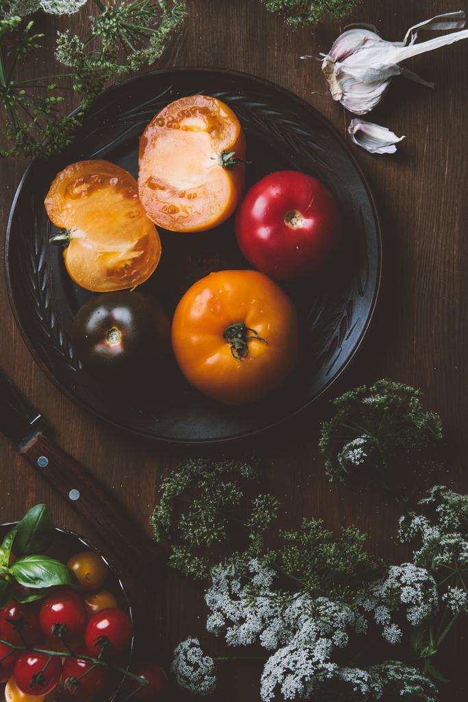 pohled shora rajčat na keramické desce s nožem na dřevěné pozadí s petrželkou květy - Fotografie, Obrázek