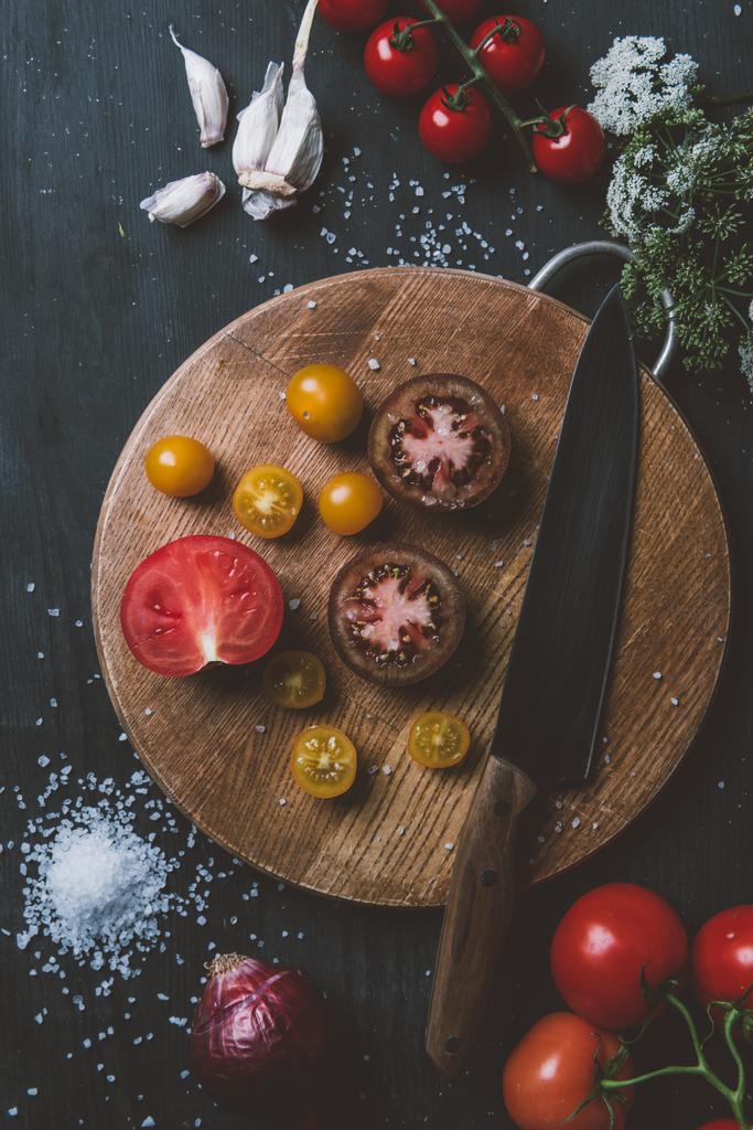 vista superior de los tomates príncipe negro y tomates cereza amarilla en la tabla de cortar con cuchillo, ajo y sal
   - Foto, Imagen