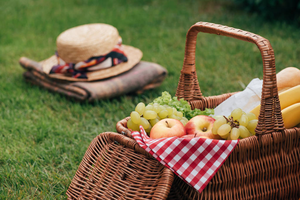вкусные фрукты в корзине на зеленой траве на пикнике, шляпа и одеяло на заднем плане
 - Фото, изображение