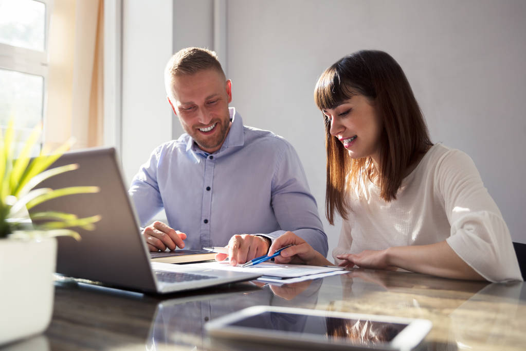 zwei glückliche Geschäftsleute, die mit Laptop auf dem Schreibtisch an Dokumenten arbeiten - Foto, Bild