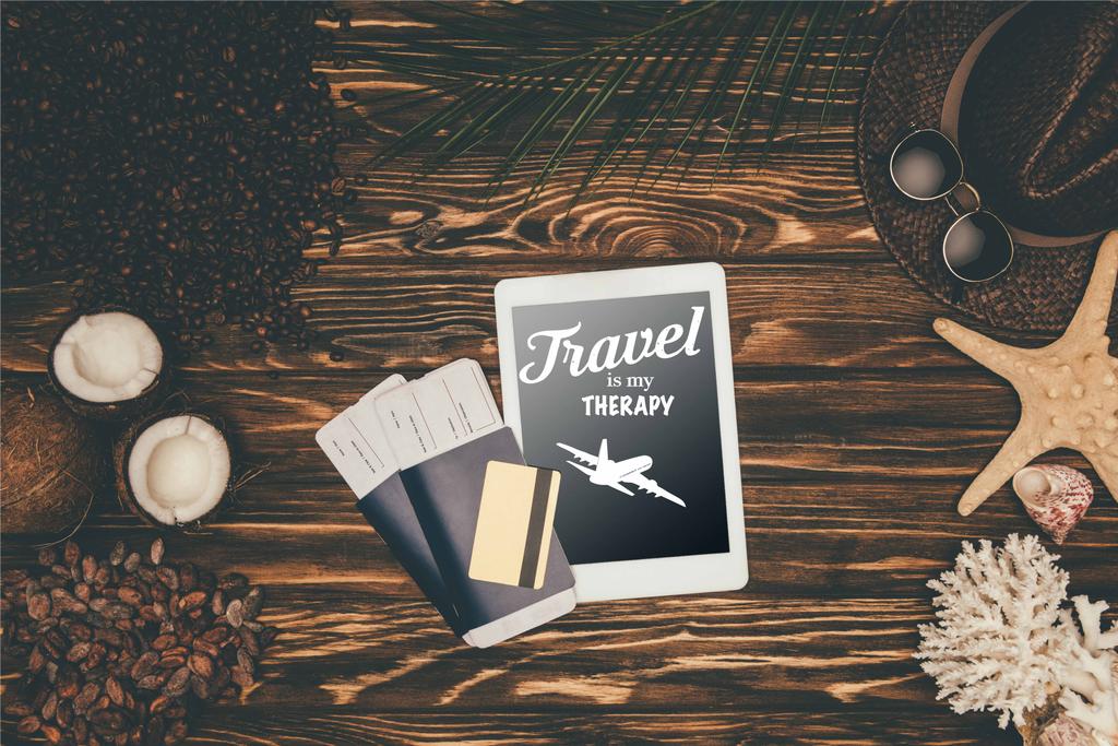 Top uitzicht van kaartjes voor digitale tablet en vlucht omgeven met verschillende tropische reizen kenmerken van houten ondergrond met "reizen is mijn therapie" belettering  - Foto, afbeelding