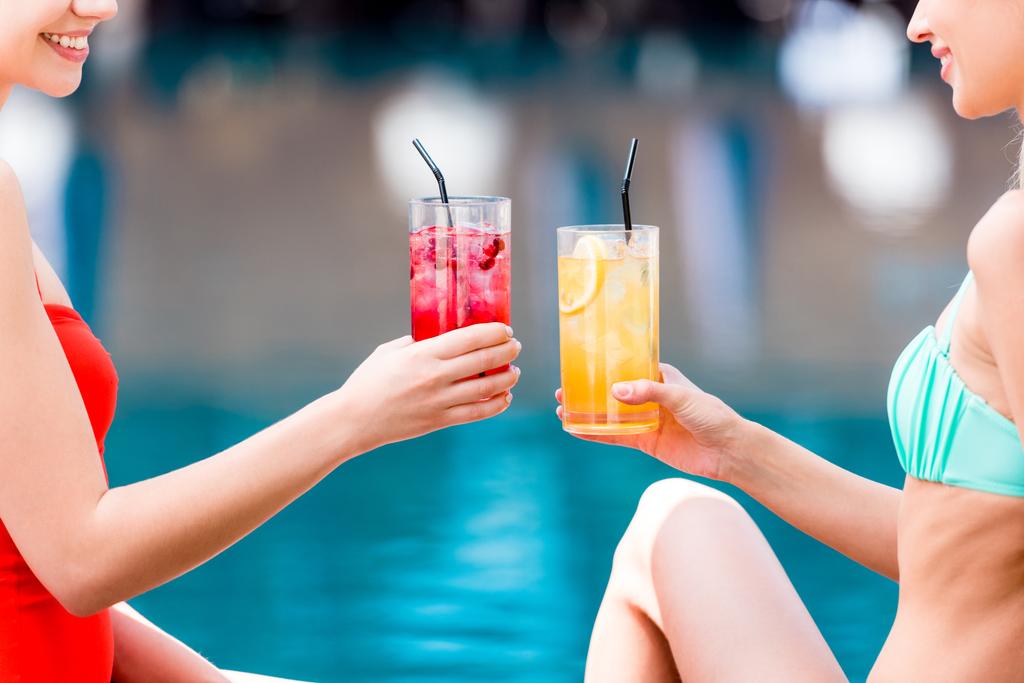 bijgesneden schot van jonge vrouwen rammelende glazen cocktails bij zwembad - Foto, afbeelding