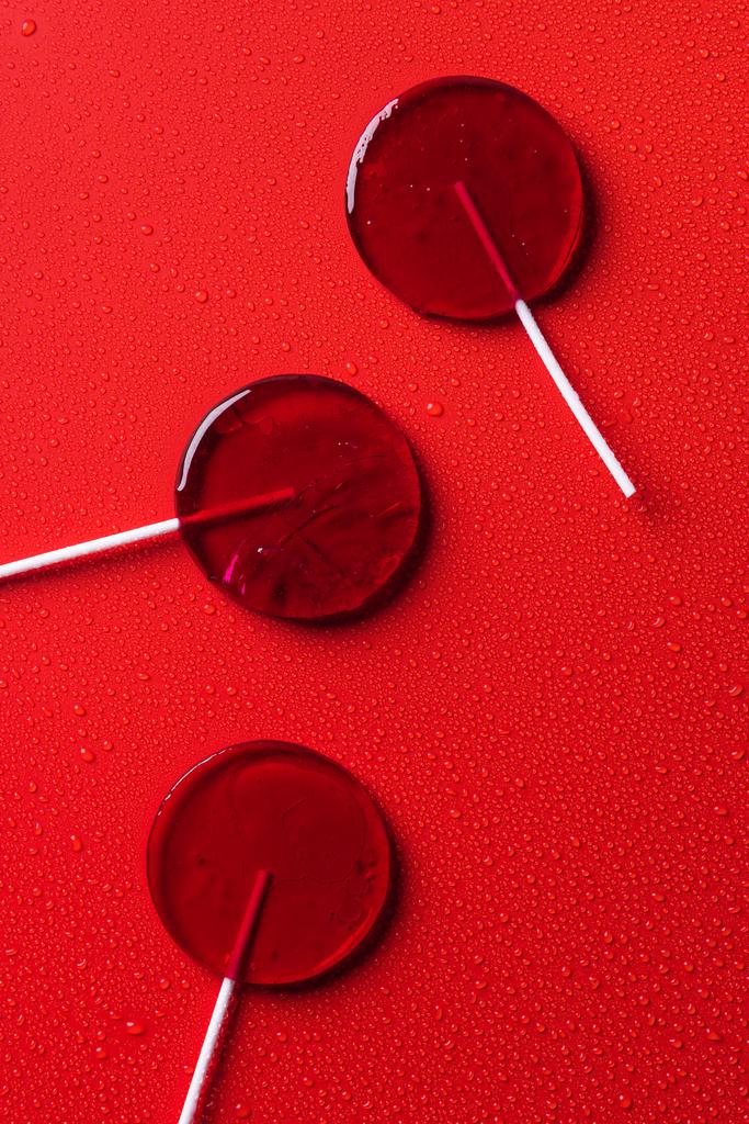 top view of three lollipops on red surface with water drops - Photo, Image