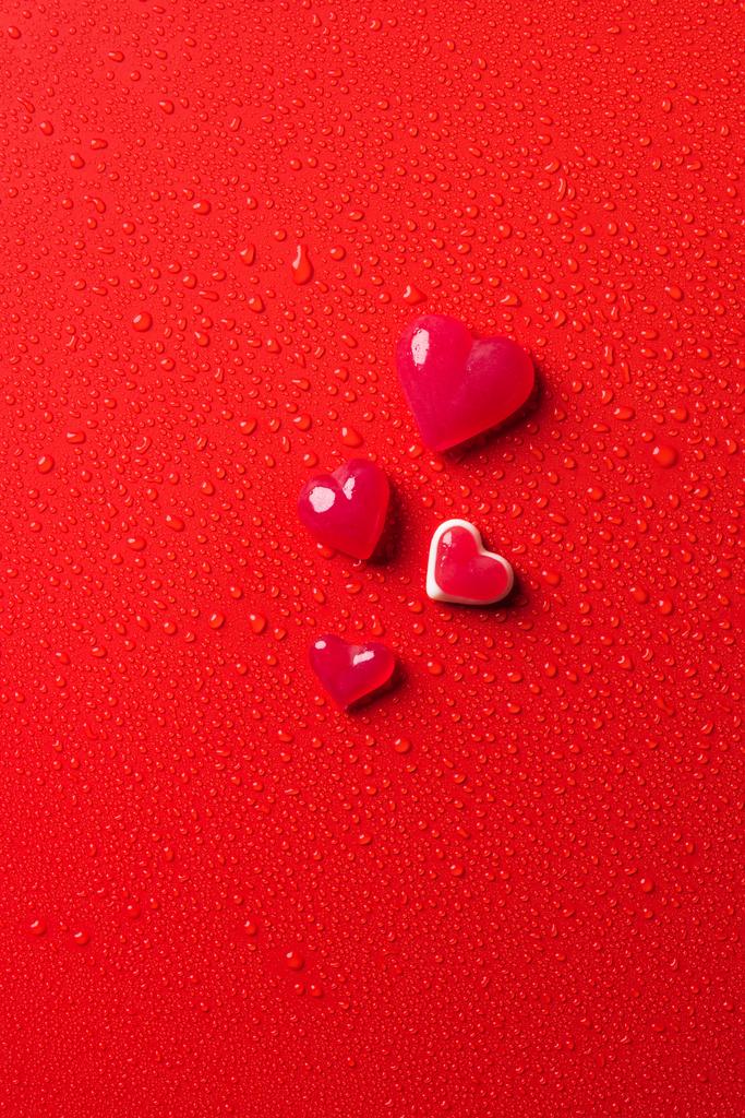 top view of heart shaped candies on red surface with water drops - Photo, Image