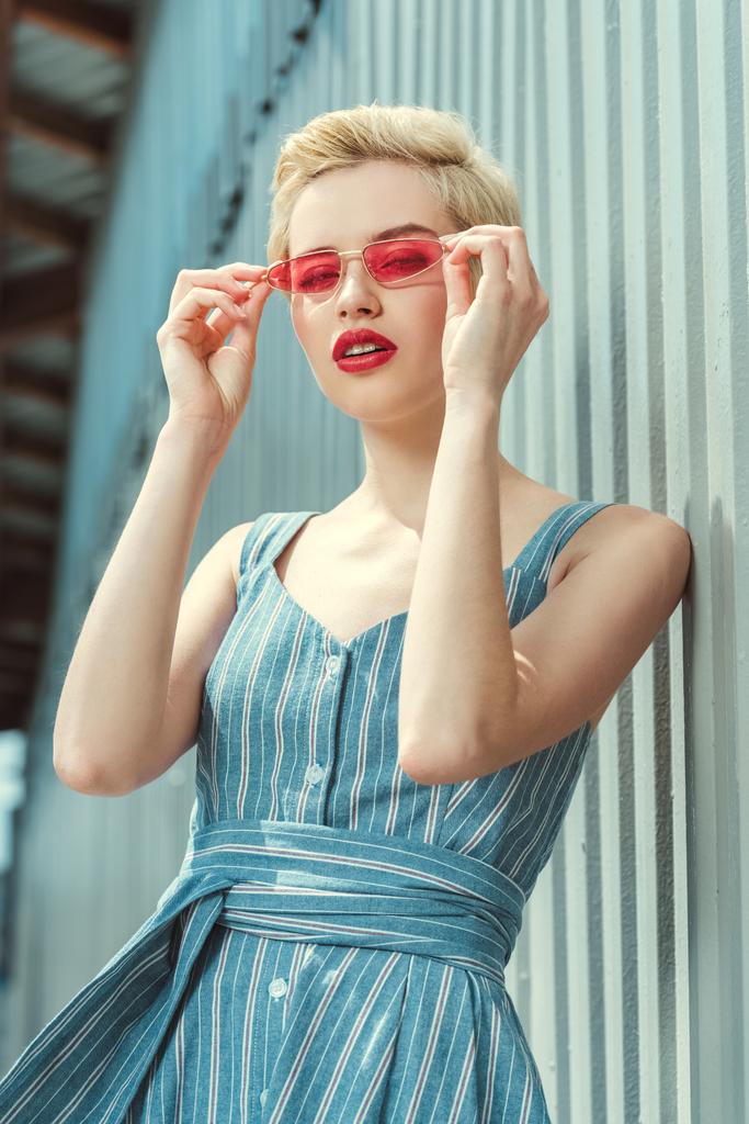 tyylikäs tyttö lyhyet hiukset poseeraa trendikäs mekko ja vaaleanpunainen aurinkolasit
 - Valokuva, kuva
