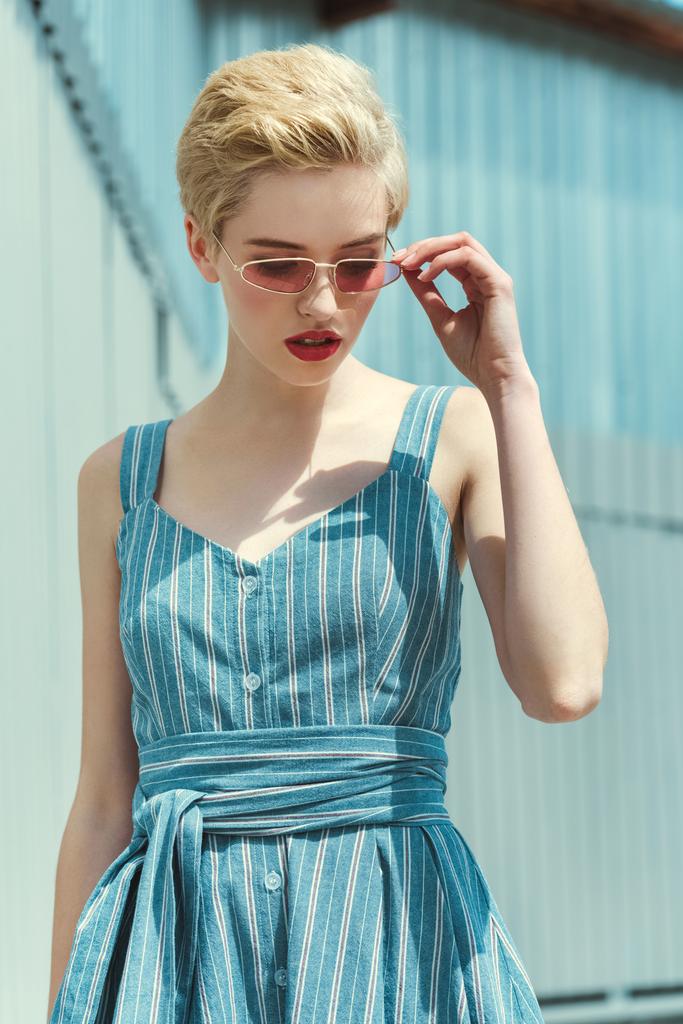 elegáns lány pózol trendi kék ruha és rózsaszín napszemüveg, rövid haj - Fotó, kép