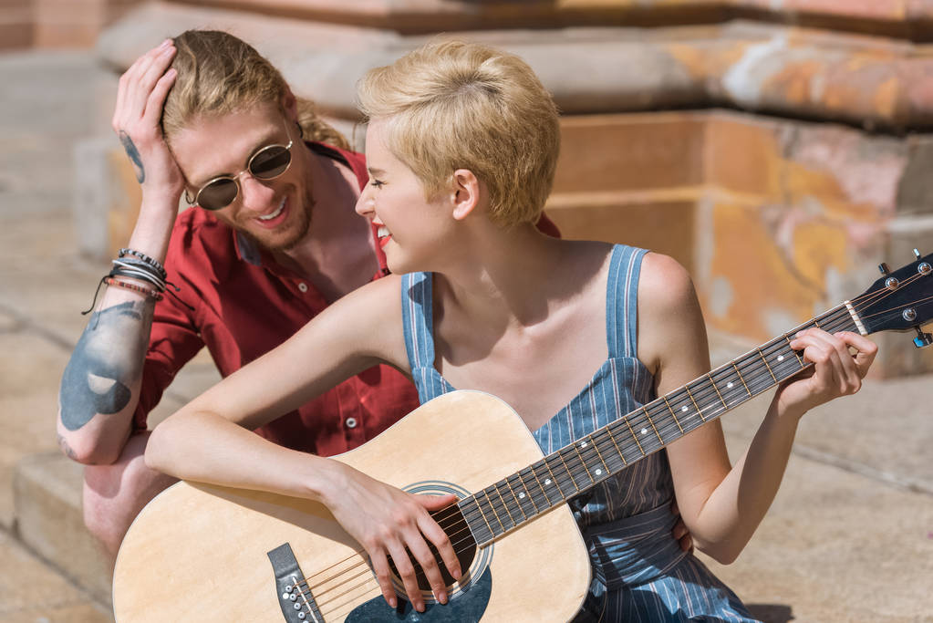 hymyilevä tyylikäs tyttöystävä soittaa kitaraa poikaystävä kadulla
 - Valokuva, kuva