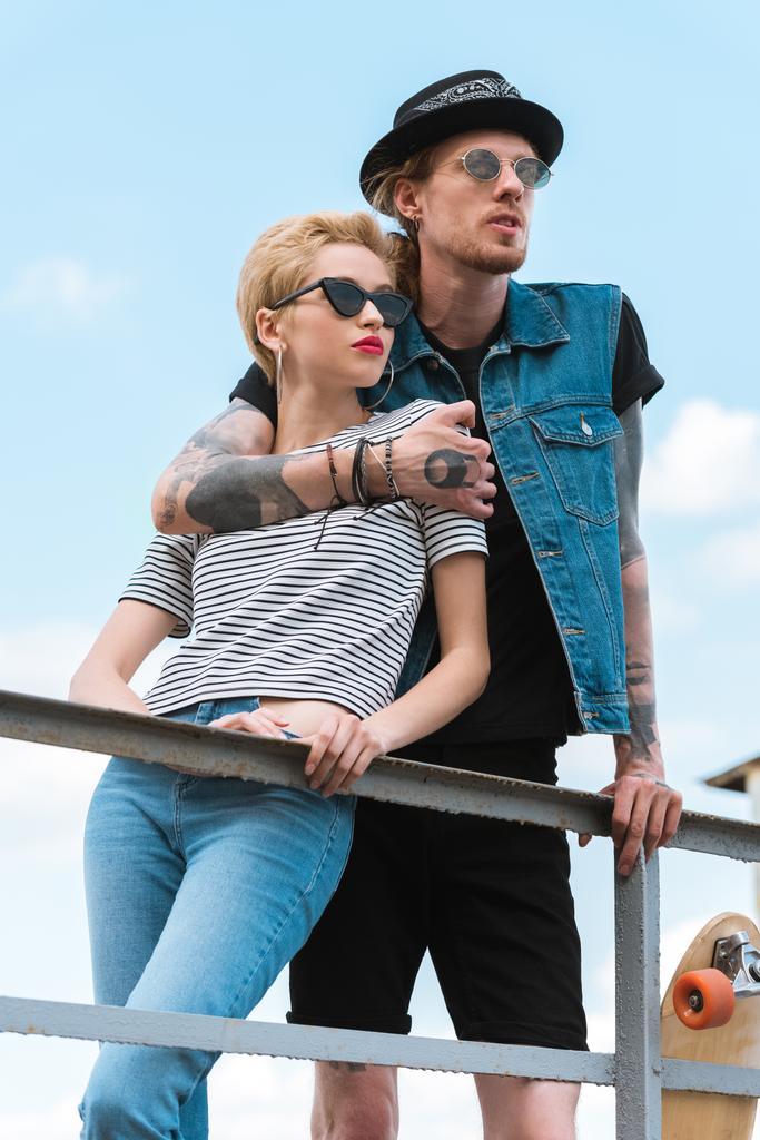 Freund mit Tattoos umarmt stylische Freundin und lehnt sich an Geländer - Foto, Bild