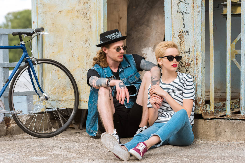 boyfriend with tattoos and stylish girlfriend sitting near wall and bicycle - Photo, Image
