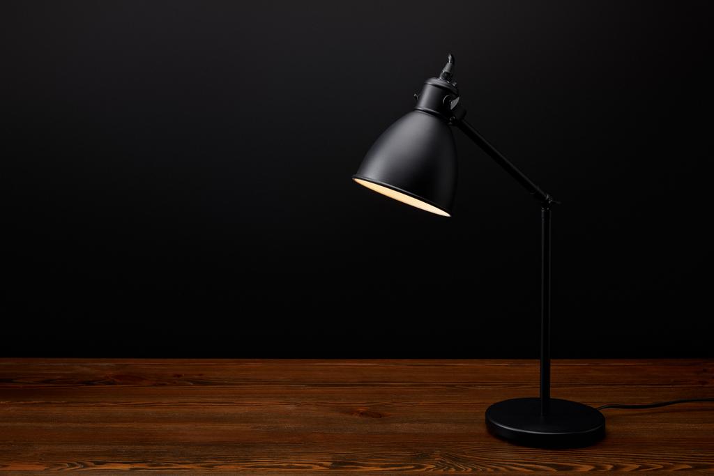 Nahaufnahme der schwarzen Lampe auf hölzerner Tischplatte auf schwarzem Hintergrund - Foto, Bild