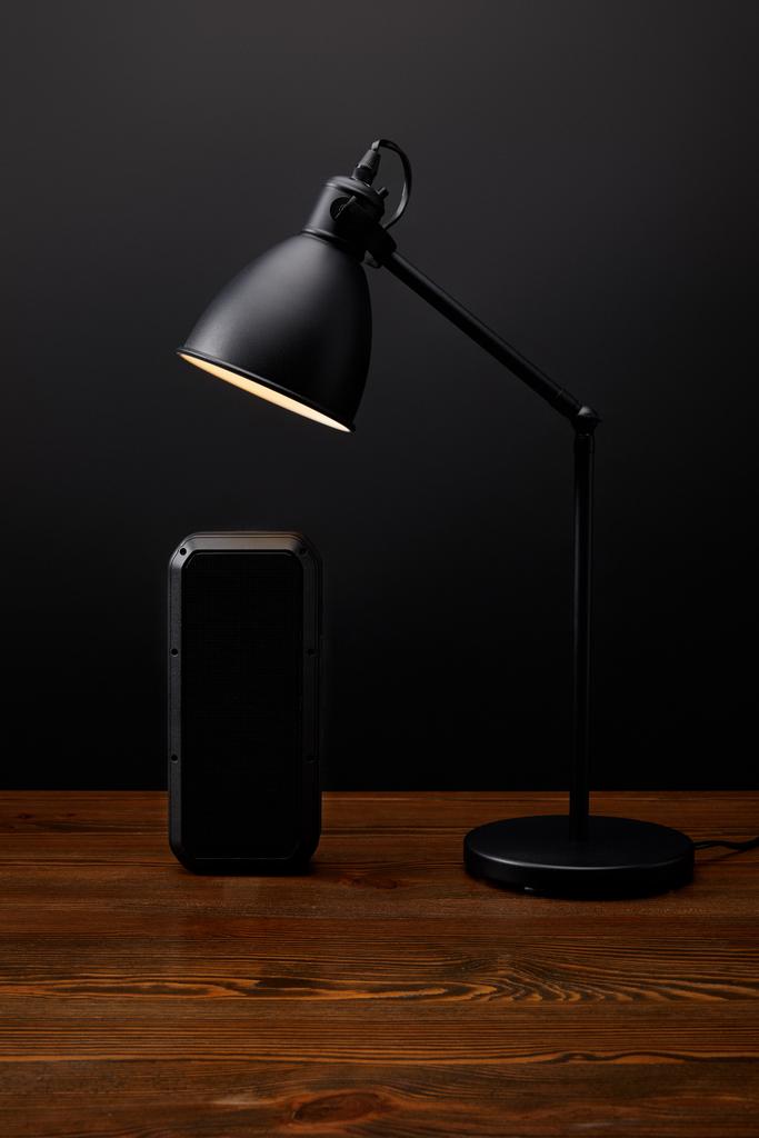закрытый вид черного аудио динамика и лампа на деревянной поверхности на черной задней стене
 - Фото, изображение