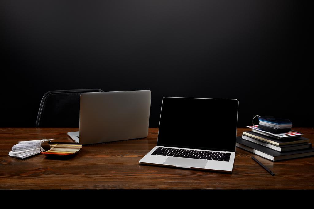 Close-up van ontwerper werkplek met laptops, notebooks en pallet op houten tafelblad op zwarte muur achtergrond - Foto, afbeelding