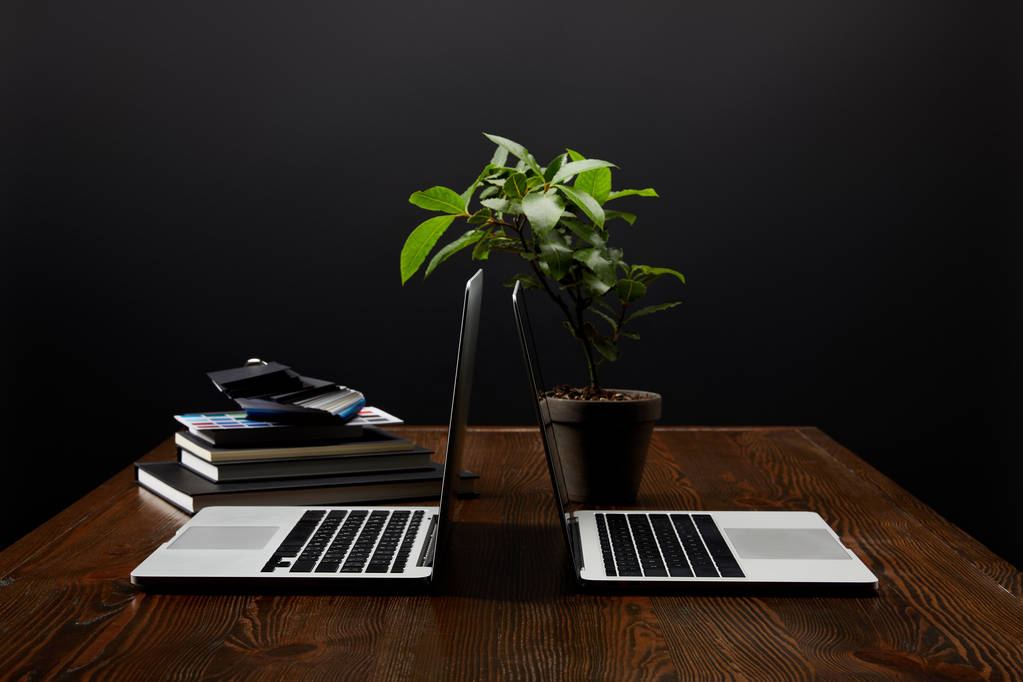 Nahaufnahme des Designer-Arbeitsplatzes mit Laptops, Notebooks und Palette auf Holztischplatte vor schwarzem Wandhintergrund - Foto, Bild