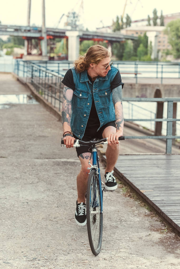 όμορφος μοντέρνος τατουάζ τον άνθρωπο ιππασία ποδήλατο στη γέφυρα - Φωτογραφία, εικόνα