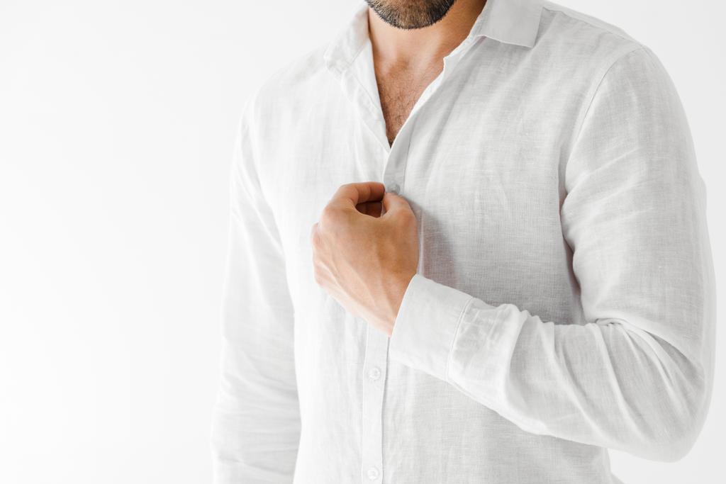 abgeschnittenes Bild eines männlichen Modells beim Aufknöpfen eines weißen Hemdes aus Leinen auf grauem Hintergrund  - Foto, Bild