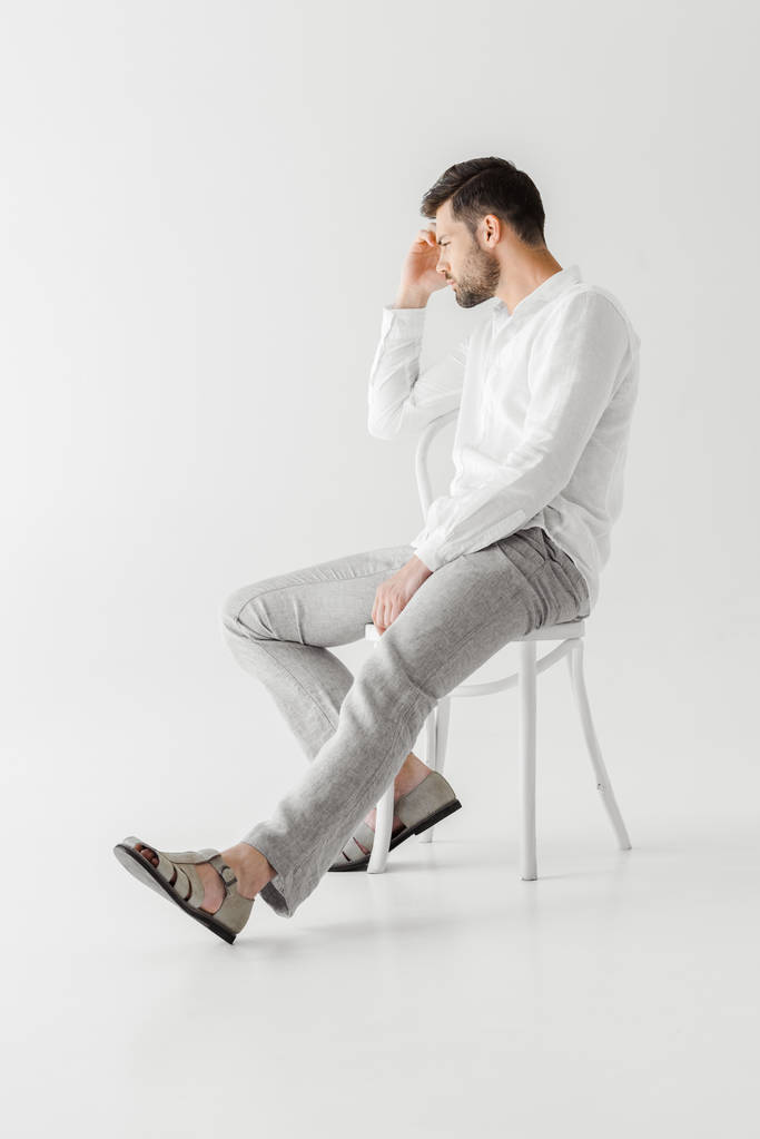 vista lateral del hombre reflexivo en ropa de lino sentado en silla aislado sobre fondo gris
  - Foto, Imagen