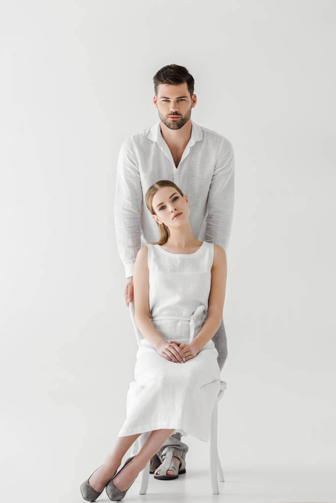 attractive woman in linen white dress sitting on chair while her boyfriend standing behind isolated on grey background  - Photo, Image