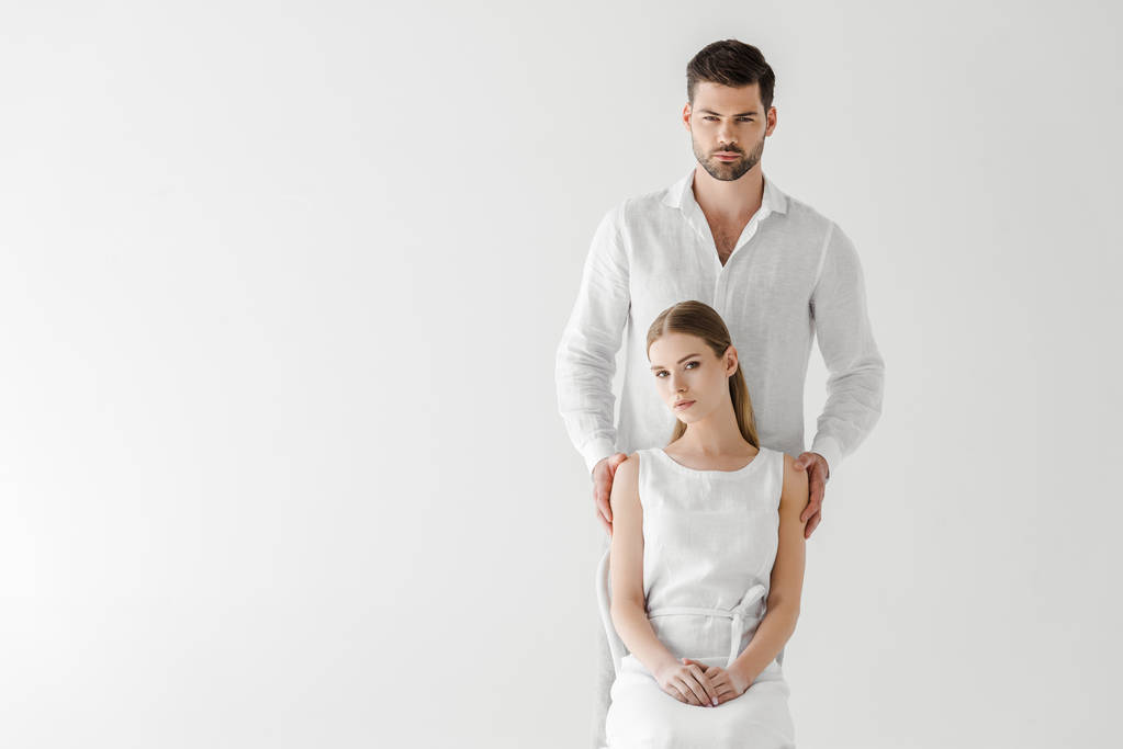 beautiful woman in linen white dress sitting on chair while her boyfriend standing behind isolated on grey background  - Photo, Image