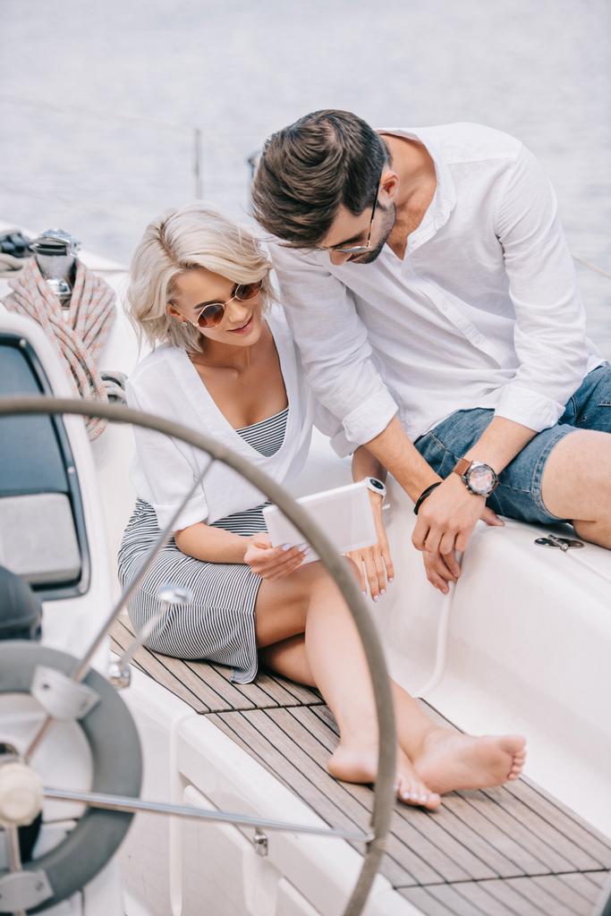 elegante giovane coppia in occhiali da sole utilizzando tablet digitale su yacht
 - Foto, immagini