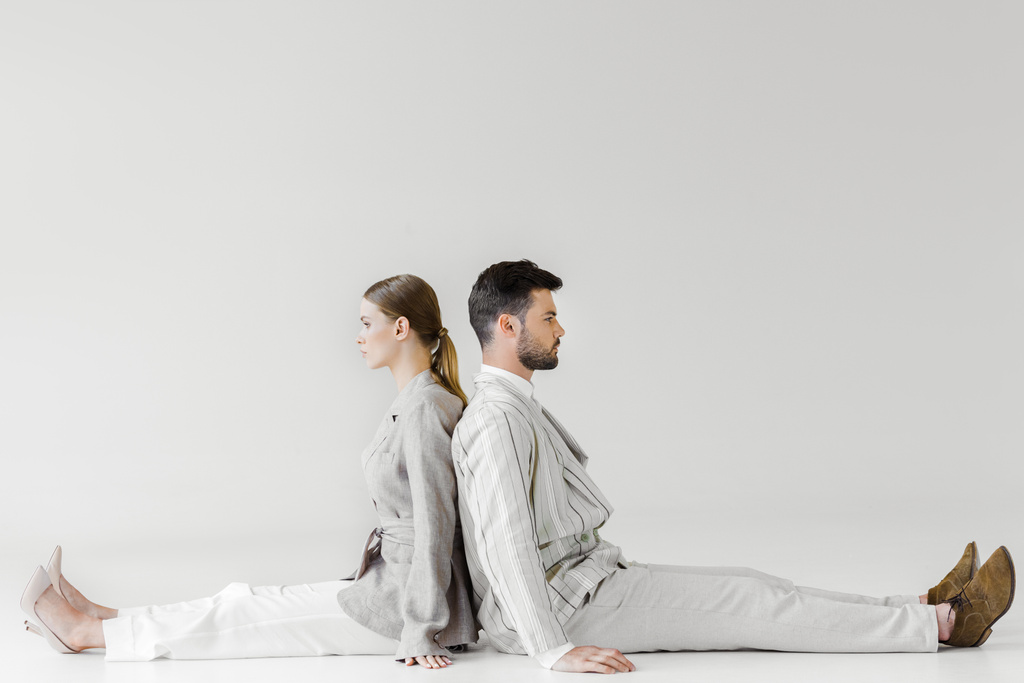 casal de modelos em roupas vintage sentado no chão e inclinando-se para trás para trás no branco
 - Foto, Imagem