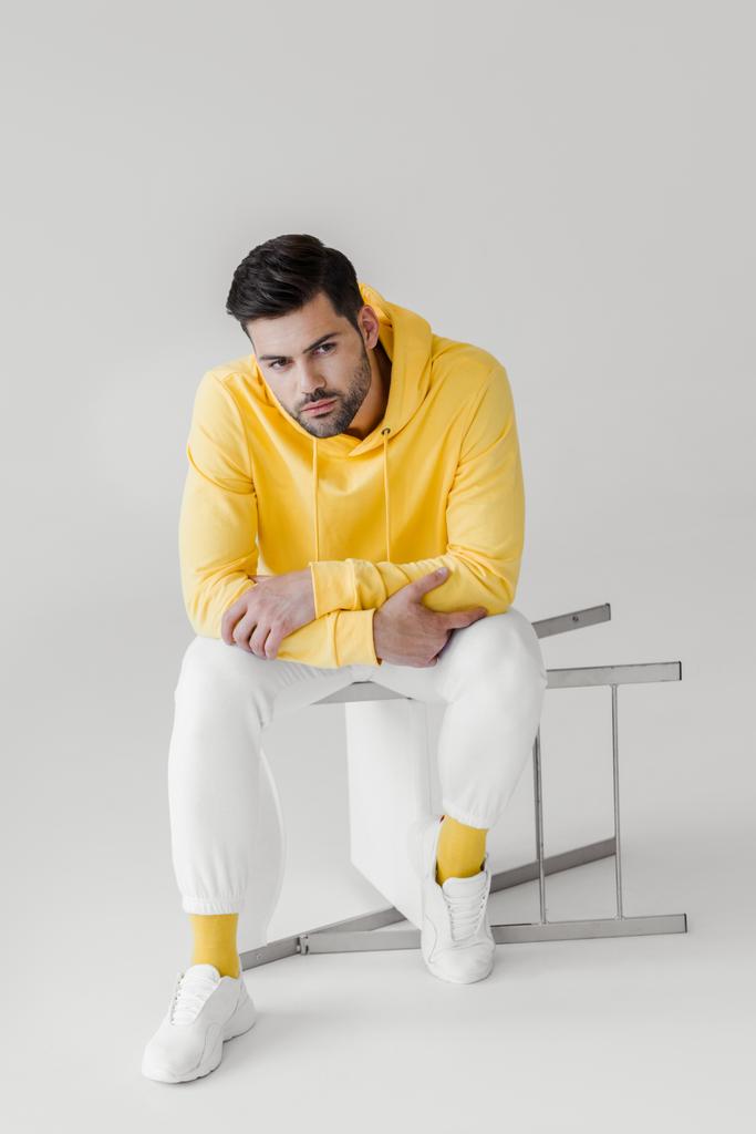 joven guapo en sudadera con capucha amarilla sentado en silla volteada en blanco
 - Foto, Imagen