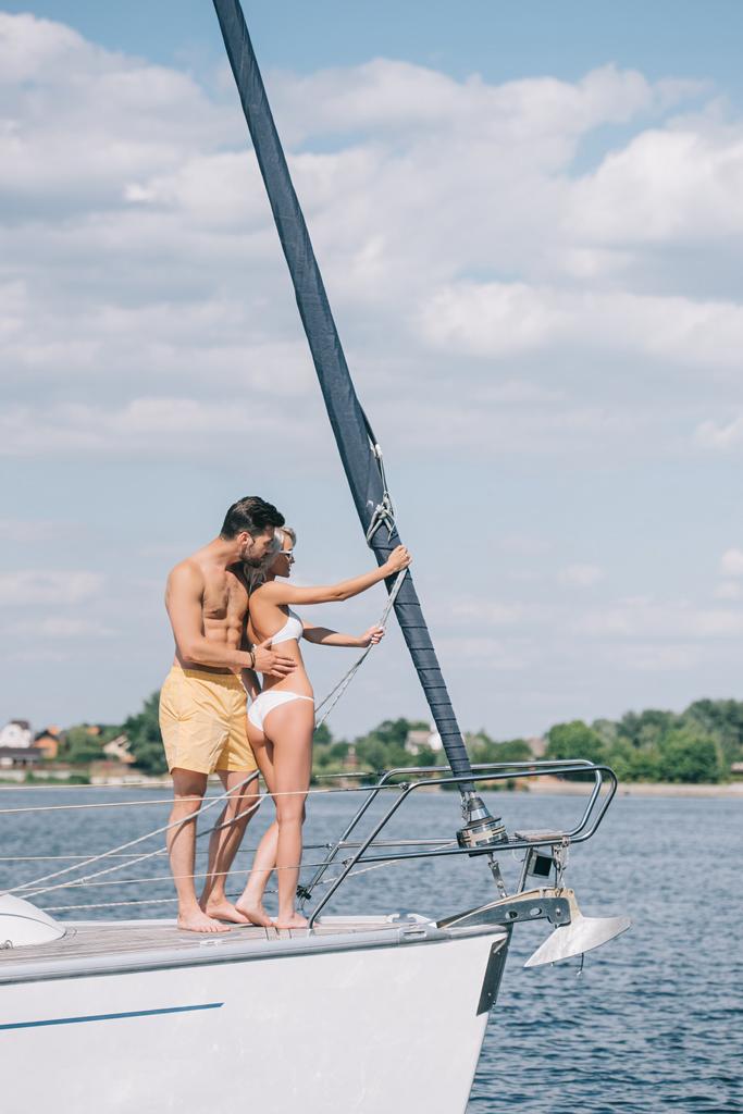 красивая молодая пара в купальниках, стоящая вместе на яхте
 - Фото, изображение