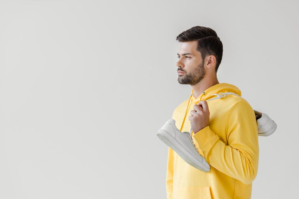 schöner junger Mann in gelbem Kapuzenpulli mit weißen Turnschuhen, die an der Schulter isoliert auf weiß hängen - Foto, Bild